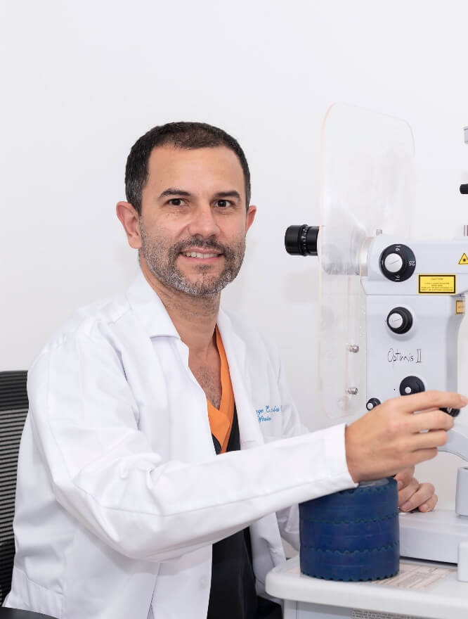 Se ve a un médico sonriendo a la cámara y a la izquierda se ve lo que se infiere como un equipo médico para la visión.