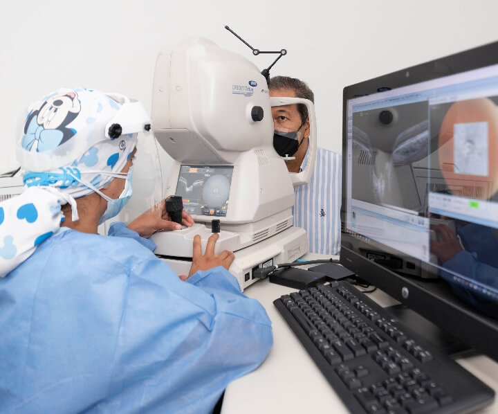 En un ambiente de consultorio médico, se ve a una profesional de la salud examinando los ojos de un paciente, usando un equipo médico. 